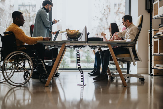 Inclusive modern office with a team of diverse professionals collaborating. A man in a wheelchair actively participates in the dynamic workspace.