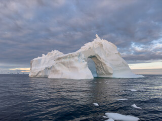 A huge high breakaway glacier drifts in the southern ocean off the coast of Antarctica at sunset, the Antarctic Peninsula, the Southern Arctic Circle, azure water, cloudy weather