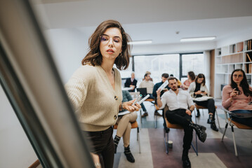 A young woman leads a presentation at a business workshop, confidently engaging with a group of professionals seated in a stylish office setting. - obrazy, fototapety, plakaty