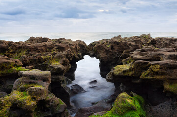 Moss-covered rocks with natural arch on shore, ideal for geology content, eco-tourism marketing, and nature-focused educational material.