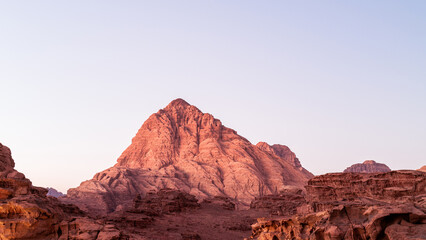 Wadi Rum, Jordan, the sun sets over a mountain with serene scenic vista, pink and red tones with blue sky. Scenery looks like Mars