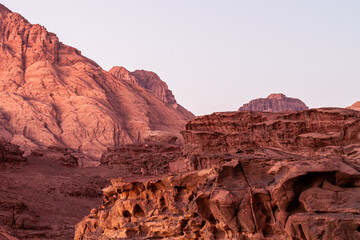 Wadi Rum, Jordan, sandstone mounds at sunset showing the erosion on the cliff edges from previous riverbed. Beautiful pink and red tones with blue sky. Scenery looks like Mars