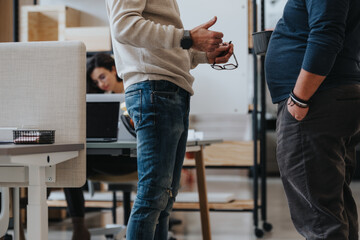 Two professionals engaging in a casual business discussion in the workspace, with a focused colleague in the background.