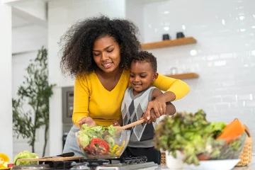 Foto op Canvas Portrait of enjoy happy love african american family mother and african little boy son child having fun help cooking food healthy eat together with fresh vegetable salad and ingredient in kitchen © Art_Photo