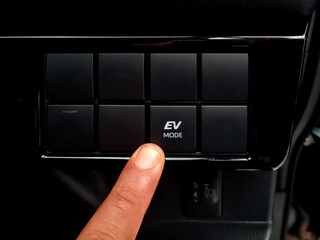 Driver's finger presses the EV button on the dashboard of a modern hybrid car. cars that use...