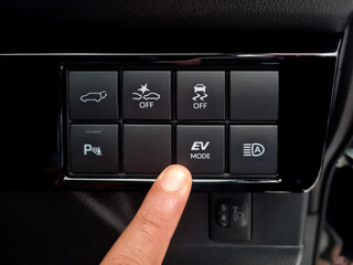 Driver's finger presses the EV button on the dashboard of a modern hybrid car. cars that use petroleum fuel but also have an electric engine or plug-in hybrid.