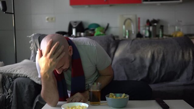 Defeated young man watching sports on the sofa celebrates a goal