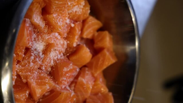 chef man hand is cutting salmon on blue board in restaurant, preparing dish for catering.cubes of fish with green spinach over ging in grill oven. close up from kitchen 4k