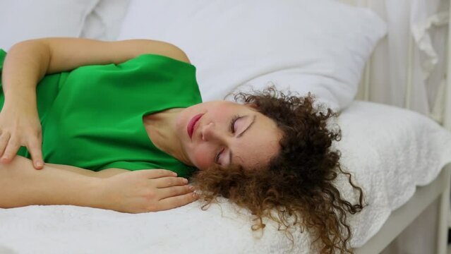Woman in green dress lies on bed and pats her hand