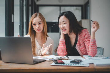 Engaged and enthusiastic businesswomen working together on a project, using a laptop in a modern office setting.