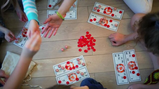 Several children play bingo with red chips on parquet floor