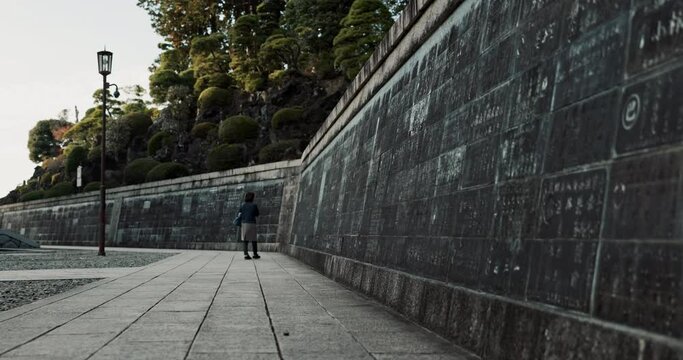 Woman at temple in Japan, walking at wall and reading calligraphy at Naritasan Shinshoji. Japanese culture, spiritual history and carved writing on sidewalk with travel adventure, zen and sightseeing