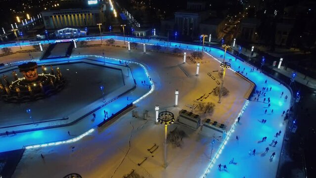Square with crowd of people get fun on ice rink around fountain