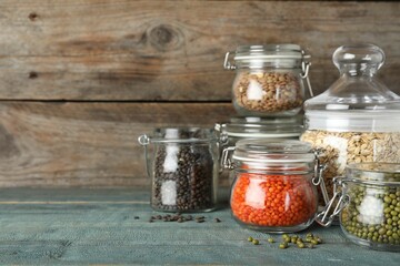Different types of legumes and cereals in glass jars on blue wooden table, space for text. Organic...