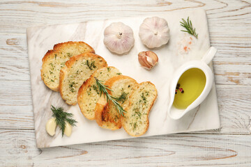 Tasty baguette with garlic, dill, rosemary and oil on white wooden table, top view