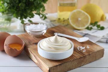 Fresh mayonnaise sauce in bowl and ingredients on white wooden table