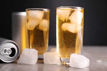 Tasty energy drink with ice cubes in glasses and aluminium cans on grey table, closeup