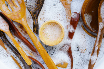 Wooden kitchenware in water and bubbles of dishwashing liquid - obrazy, fototapety, plakaty
