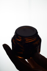 Close-up of a mockup of a glass jar with skin care oil in a woman hand on a white background.