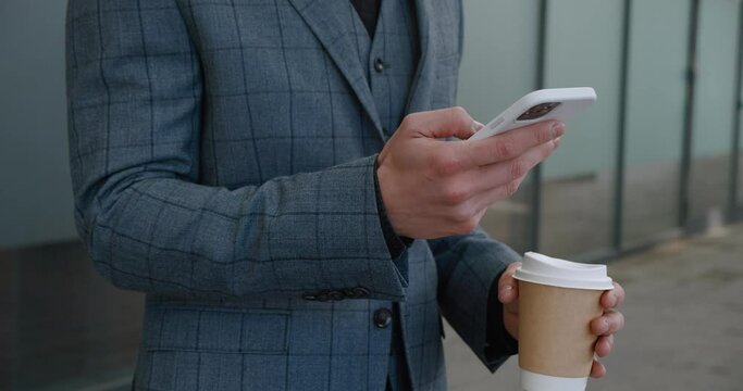 Close-up view of man's hands in suit holding coffee cup while checking his phone Coffee cup symbolizes brief respite from work. Each sip from coffee cup blends leisure with business.