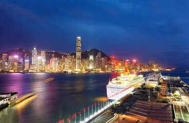 Obraz premium Night scenery of Hong Kong with a skyline of crowded skyscrapers by Victoria Harbor, a luxury cruise liner parking by the pier of Harbour City and lights of high-rise buildings glistening in twilight