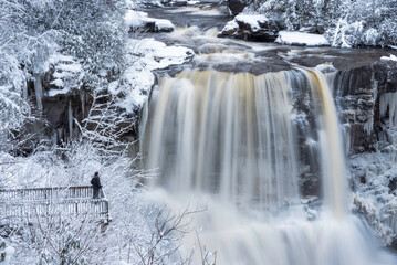 A man poses on viewing platform in front of Blackwater Falls on a winter day in Davis, West Virginia.