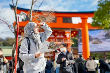 Gordijnen Travel, muslim, Two Asian female tourists of different religions friends visitor learning about history of fushimi inari shrine in travel book while walking through senbon torii path in Kyoto Japan. © maya1313