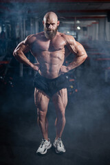 Fototapeta na wymiar Muscular bald man posing in shorts. Bodybuilder showing off his shape in the gym. 