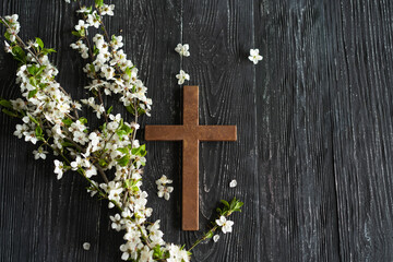 Cross with flowers on a wooden background with the inscription Christ is Risen. Easter concept. Cross symbolizing the death and resurrection of Jesus Christ