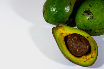 Half an avocado is arranged with another avocado decoration on the right side with a plain white...