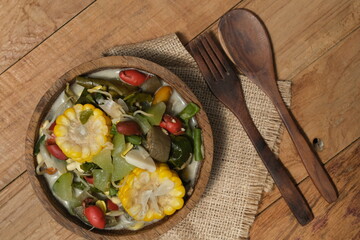 Sayur lodeh or vegetables with coconut milk soup is traditional Indonesian culinary food from Java in white bowl served on coconut tree trunk bowl, on a wooden table. Selective focus. Top view. 