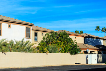 Typical view from a public parking of a gated Arizona housing residential community with a high block fence, stucco finished houses, palms and ripe yellow citrus fruits on a warm winter morning