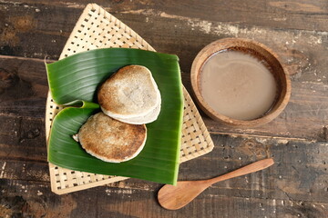 Serabi Surabi Kocor is traditional Javanese snack made of rice flour, coconut milk, pandanus leaves, and palm sugar. Served in bamboo woven basket on wooden table. Flat lay. Indonesian food. 