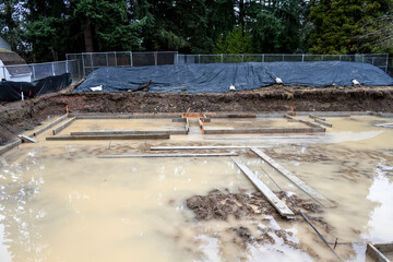 Under construction, residential house foundation dug out and framing started, flooded with rainwater in a wet environment
