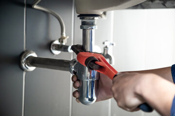 Plumber uses wrench to repair water pipe under sink There is maintenance to fix the water leak in the bathroom.with red wrench, plumbing install concept. - obrazy, fototapety, plakaty