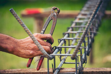Construction Worker hands using pincer pliers iron wire. Outdoor Worker using wire bending pliers, construction work. Men hands bending cutting steel wire fences bar reinforcement of concrete work - obrazy, fototapety, plakaty