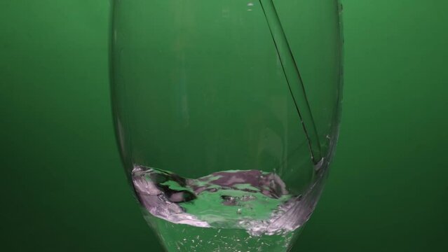 Pouring water in transparent spinning glass filling up slow motion on green background