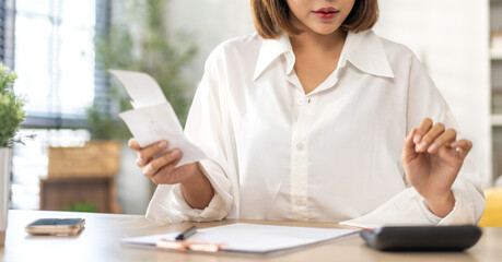 Smiling asian woman using calculator and calculate bills on laptop, paying bill, credit card, finance, tax, vat, credit card,  payment, tax refund, budget, debt, money.financial and accounting concept