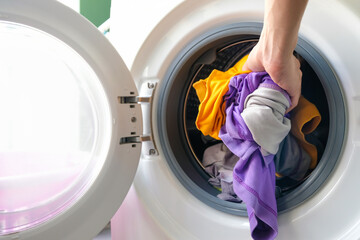 A woman opens the front door of a washing machine and puts clothes into the washing machine to...