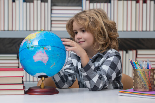 School boy looking at globe in library, geography lesson. School child student learning in class, study english language at school. Elementary school child. Portrait of funny pupil learning.
