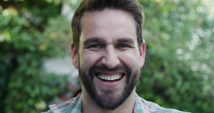 Man, face and happy with closeup in garden, pride and confidence by plants, trees and holiday. Excited guy, person and smile outdoor with portrait, green backyard or home in spring in San Francisco