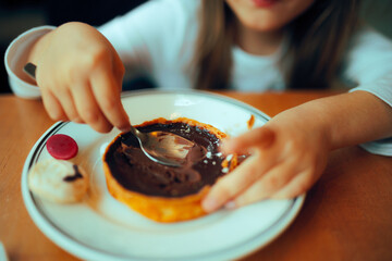 
Little Girl Eating a Chocolate Cake in a Restaurant  
Child enjoying a pastry tart with coca cream
