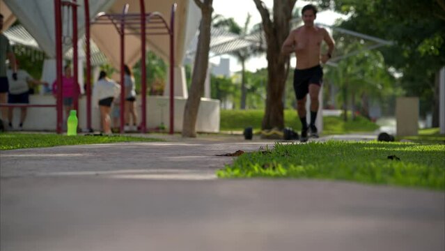 Slow motion of a shirtless latin male athlete finishing his running routine towards the camera at the park