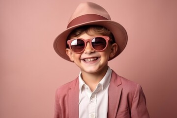 Portrait of a cute little boy in a hat and sunglasses on a pink background.