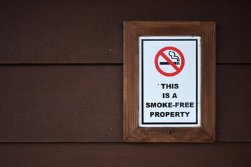 This is a smoke free property sign, framed, mounted on wooden siding.