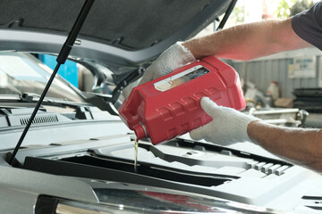 Fototapeta premium Maintenance at a car service station.Oil change in the car engine. An auto mechanic holds a canister of automotive synthetic oil.