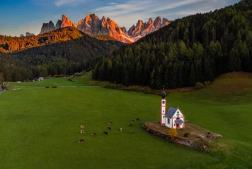 Photo sur Plexiglas Dolomites Val Di Funes, Dolomites, Italy - Aerial view of the beautiful St. Johann Church (Chiesetta di San Giovanni in Ranui) at South Tyrol with cows and Italian Dolomites in warm sunset colors at background