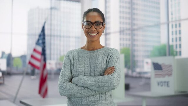 Portrait of a Beautiful African American Female Posing with Big Bright Smile with American Flag in the Background. Successful Young Black Woman Looking at Camera, Standing with Crossed Arms