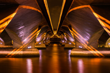 Golden symmetrical lights under a modern concrete bridge over a river