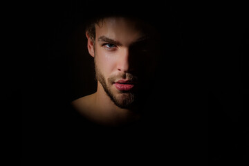 Sexy gay studio portrait. Silhouette portrait of a young man. Man in shadows. Upper body man silhouette. Black studio background. Young man close-up portrait, with shadow on studio lowkey. Studio shot